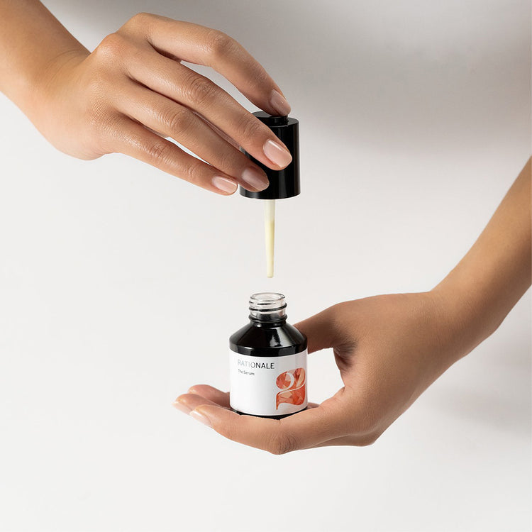 Hands hold an open RATIONALE The Serum dropper bottle