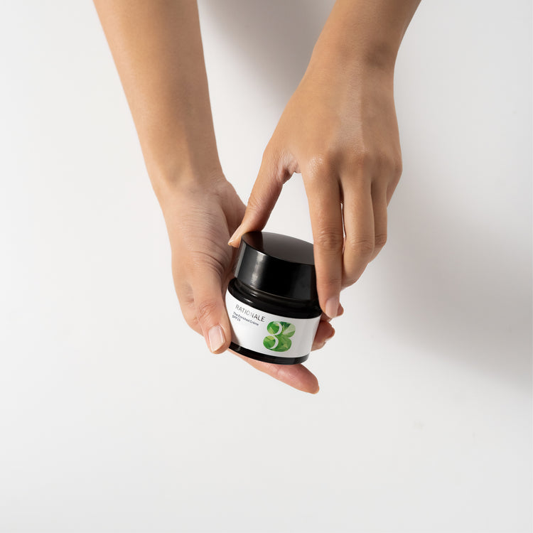 Hand holding a small jar of skincare cream with a dark lid.