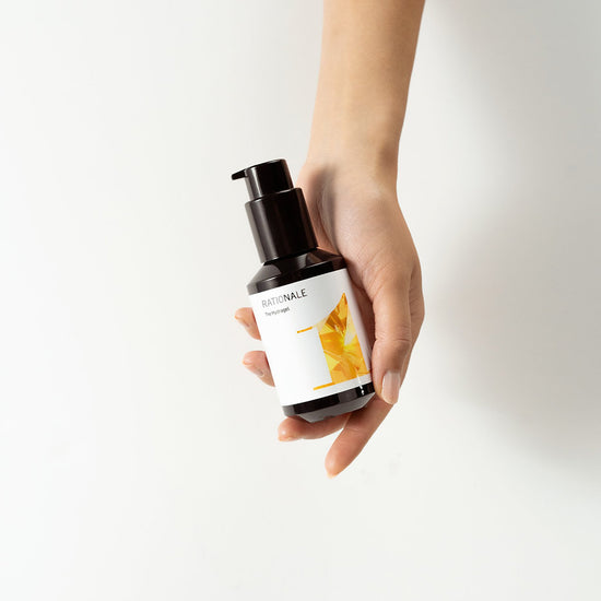 Hand holds a dark bottle with a pump, RATIONALE The Serum