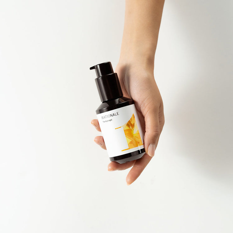 Hand holds a dark bottle with a pump, RATIONALE The Serum