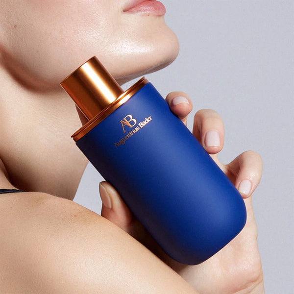 Blue perfume bottle with bronze cap held by a person against a neutral background
