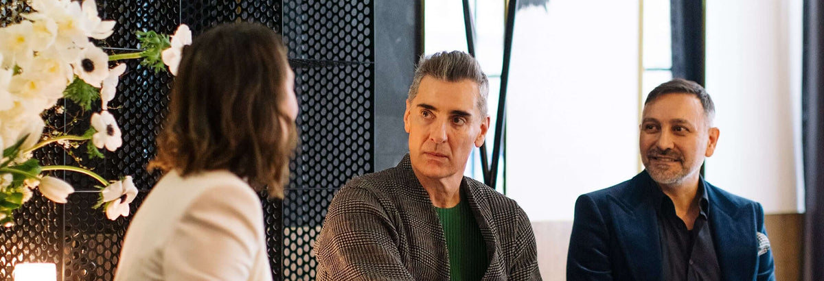 Rationale x All Saint Clinic event, founders seated in a modern indoor setting, with facing the interviewer. The man on the right wears a dark blue blazer over a black shirt, the center man wears a textured brown jacket over a green shirt, and the woman wears a light beige top.