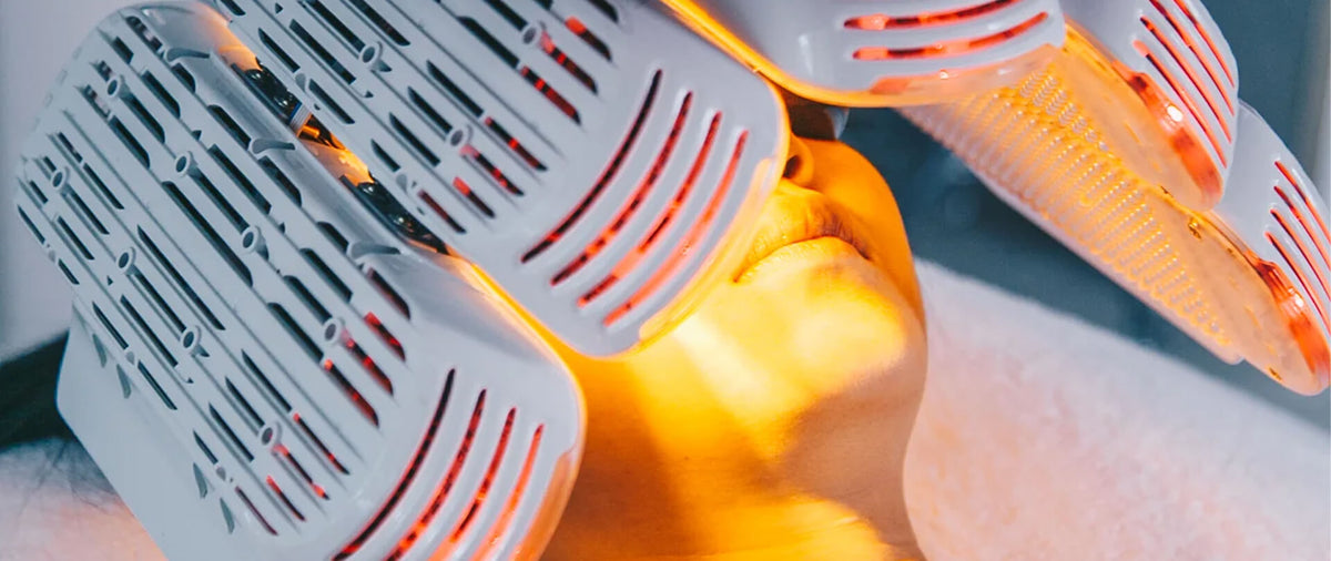 A close-up of the Saint Healing light therapy panel emitting warm orange light onto a person's face, with another panel visible in the background.